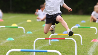 Student running and jumping over hurdles.