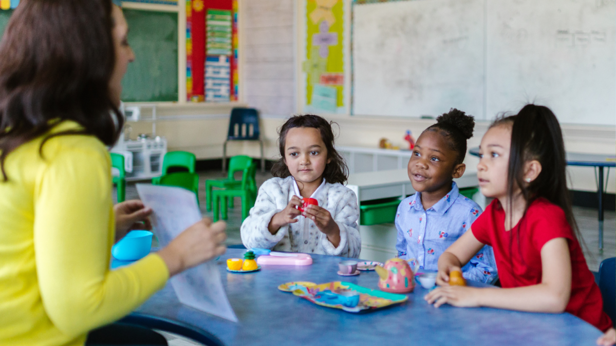 Children sitting at a rainbow table with a teacher.