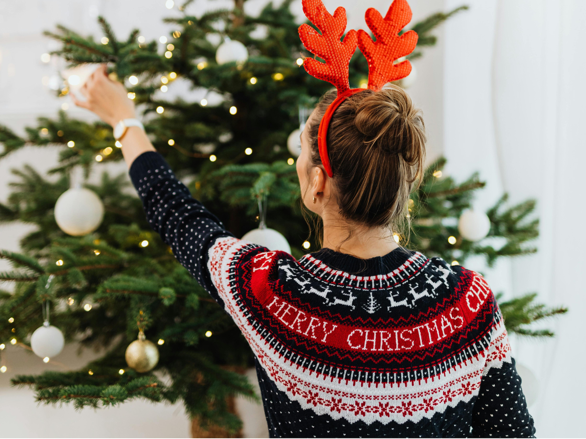 A person in a Christmas sweater decorating a Christmas tree.