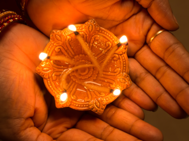 Hands holding a lit diya.