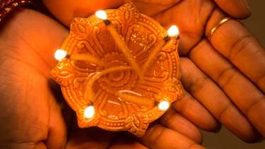 Hands holding a lit diya.