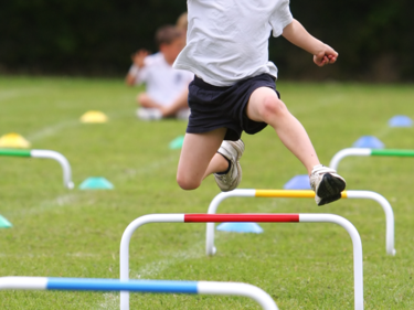 Student running and jumping over hurdles.