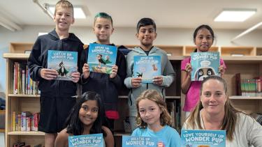 Wonder Pup Books Group Photo Six students and 1 Adult holding up books in front of them in the library.