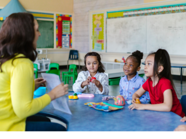 Children sitting at a rainbow table with a teacher.