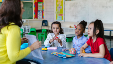 Children sitting at a rainbow table with a teacher.