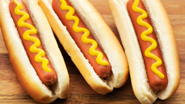 Three hot dogs with mustard on them.