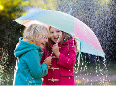 Two children under a pink and blue umbrella in the rain.