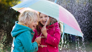 Two children under a pink and blue umbrella in the rain.