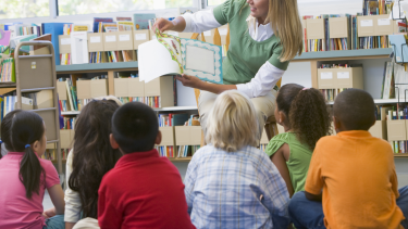 2025/2026 Kindergarten Registration Students listening to a teacher reading them a story.