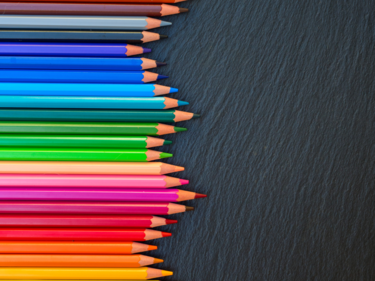 Colourful pencil crayons lined up on a chalkboard.