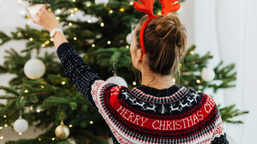 A person in a Christmas sweater decorating a Christmas tree.