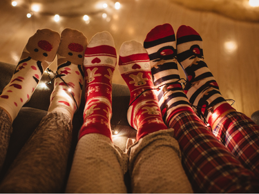 Three sets of feet in Christmas socks and pj pants with Christmas lights in the background.