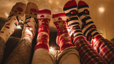 Three sets of feet in Christmas socks and pj pants with Christmas lights in the background.