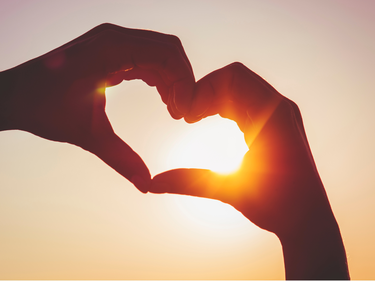 Hands making a heart shape in front of the sun.