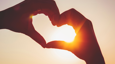 Hands making a heart shape in front of the sun.