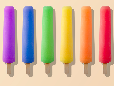 Rainbow coloured popsicles on a beige background.