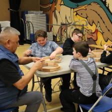 Knowledge Keeper Darren Charlie helps four grade 5 male students with their drums